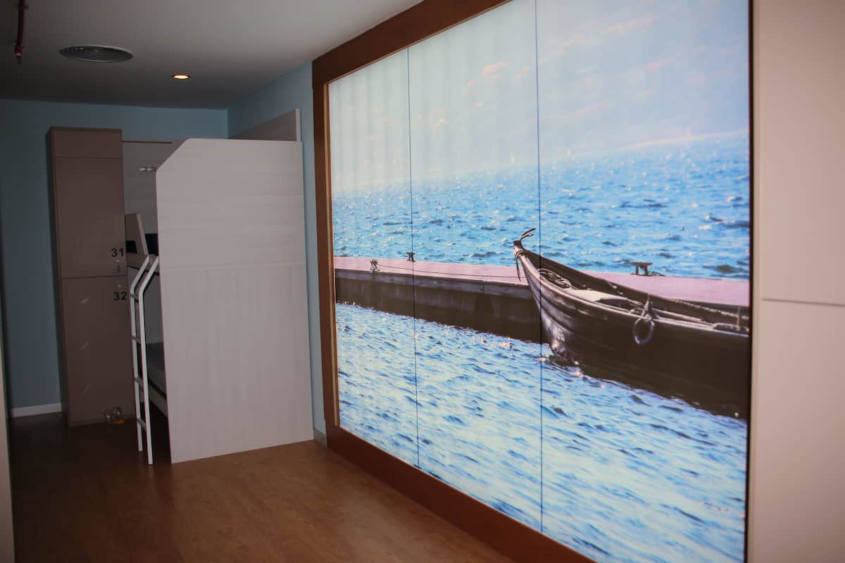 A room with a large window displaying a view of a dock and water. There is a bunk bed with a ladder and a small table.