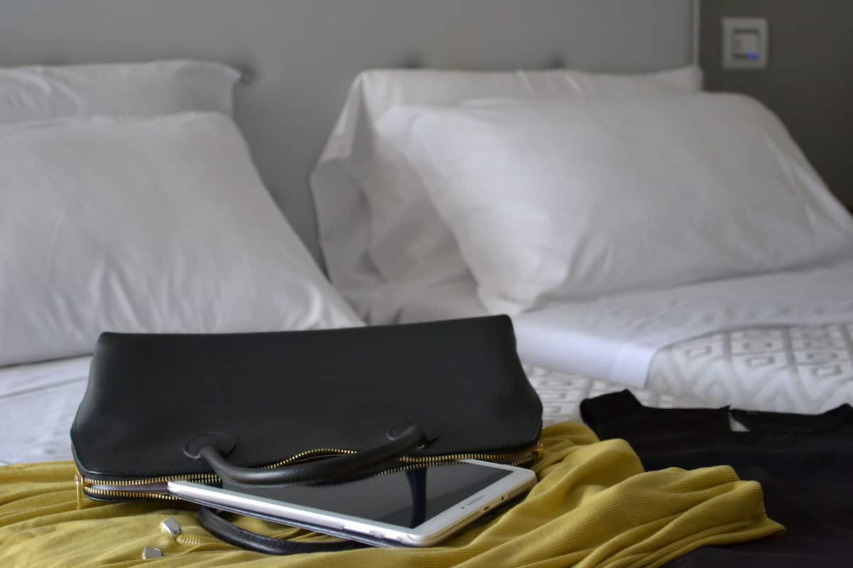 A bed with white pillows and a black bag on a yellow bedspread.
