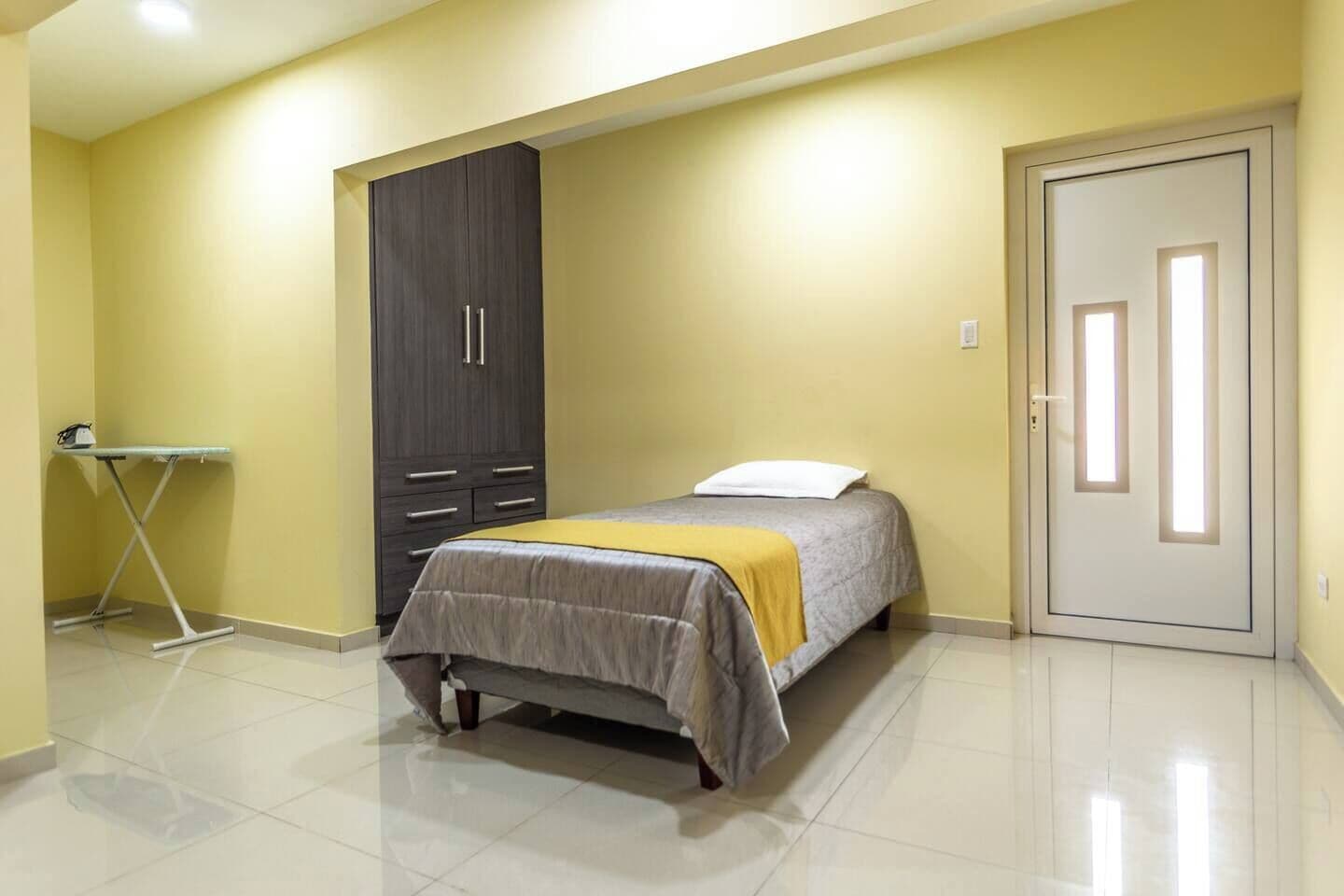 A bedroom with a bed, a wardrobe, a door, and a small table.
