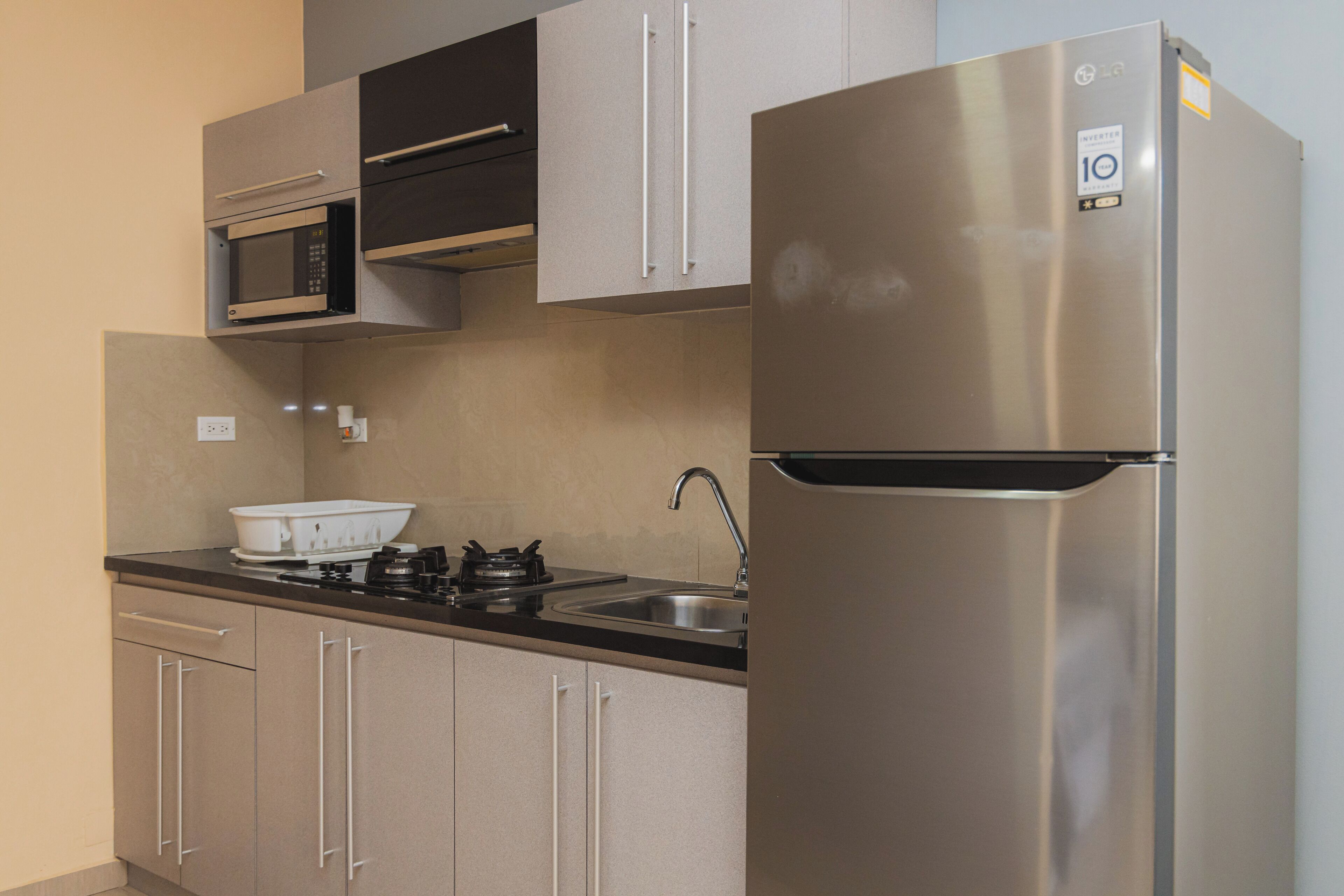 A modern kitchen with stainless steel appliances, including a refrigerator and microwave, and beige cabinetry.
