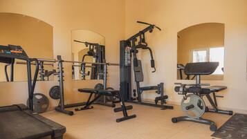 Ett gym med olika typer av träningsutrustning, inklusive en bänk, en viktbänk och ett knäböjsställ.