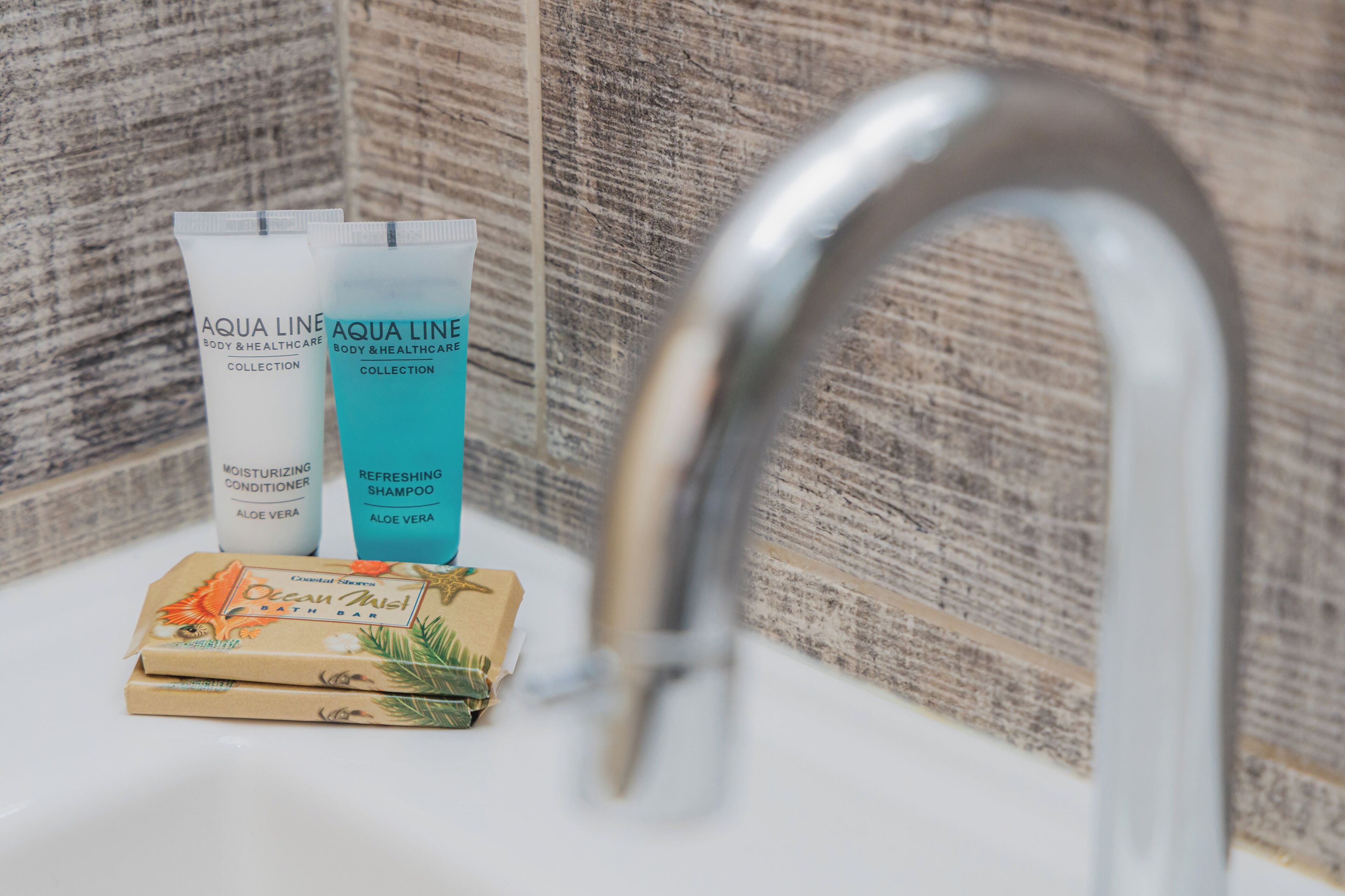 A bathroom sink with two Aqua Line body and healthcare collection products, a bath bar, and a wooden textured wall.