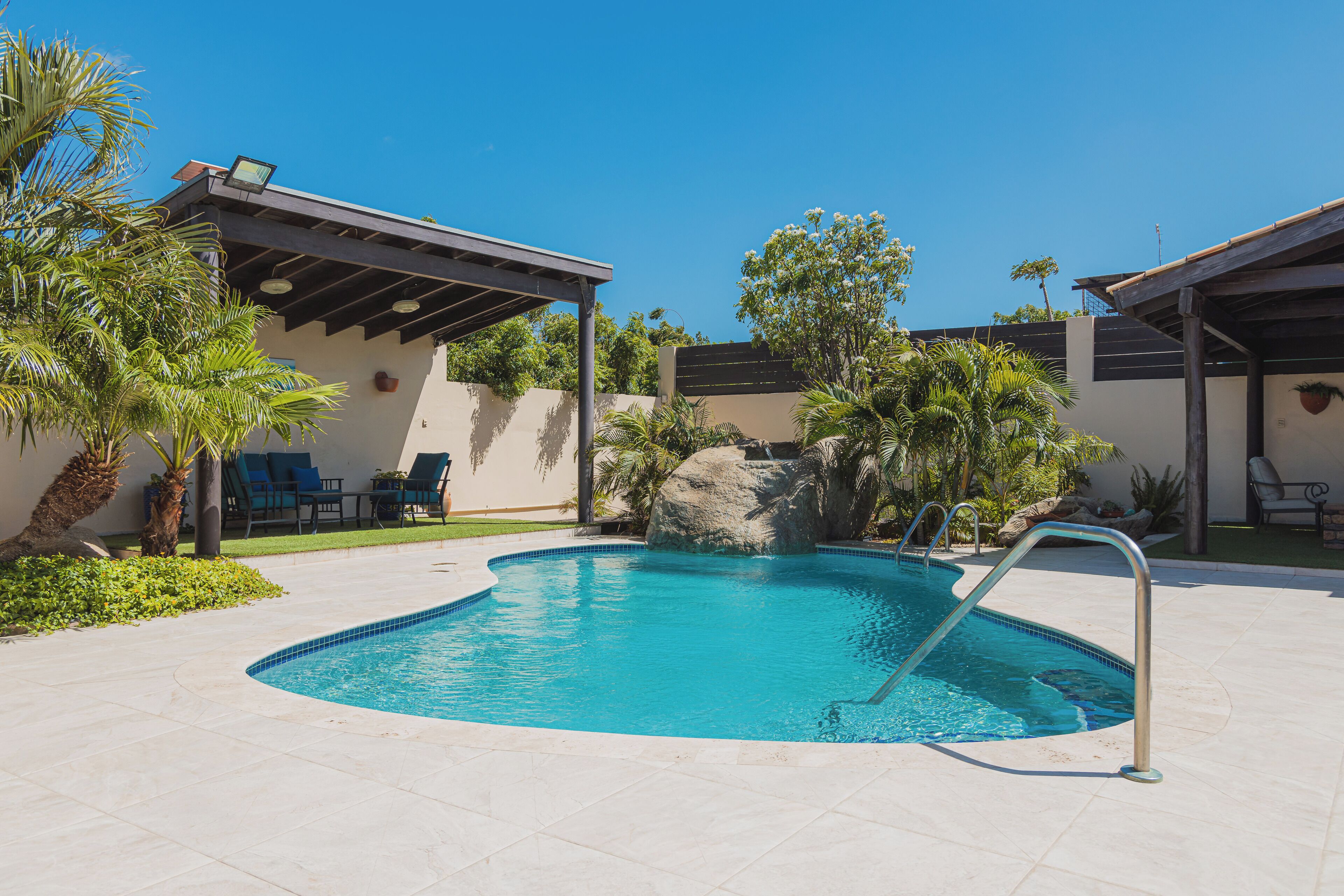 A swimming pool with a stone feature, surrounded by palm trees and lounge chairs.