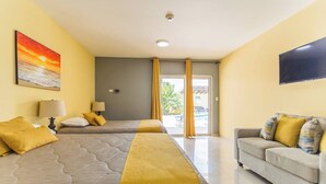 A hotel room with two beds, a sofa, a TV, and a painting of a sunset. - Juanedu Suites (Oranjestad)