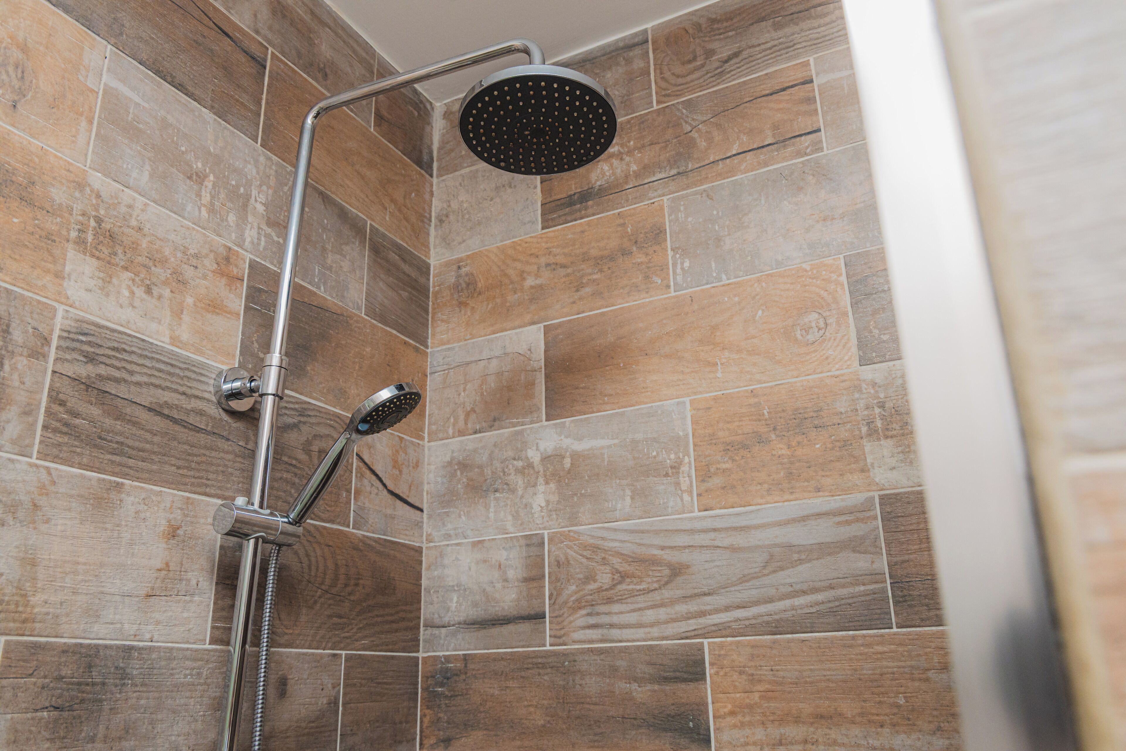 Ducha con cabezal de ducha de mano y cabezal de ducha fijo, sobre un fondo de azulejos con diseño de madera.