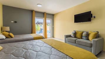 A hotel room with two beds, a sofa, a TV, and a view of an outdoor pool.