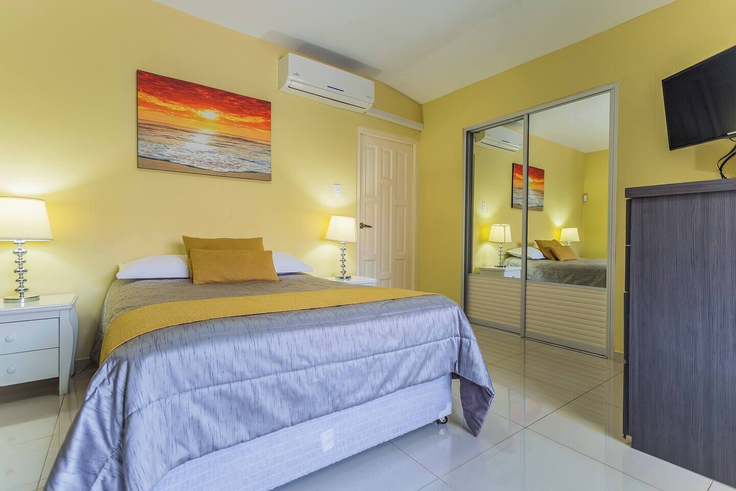 Una habitación de hotel con cama, mesitas de noche, un espejo y televisión.