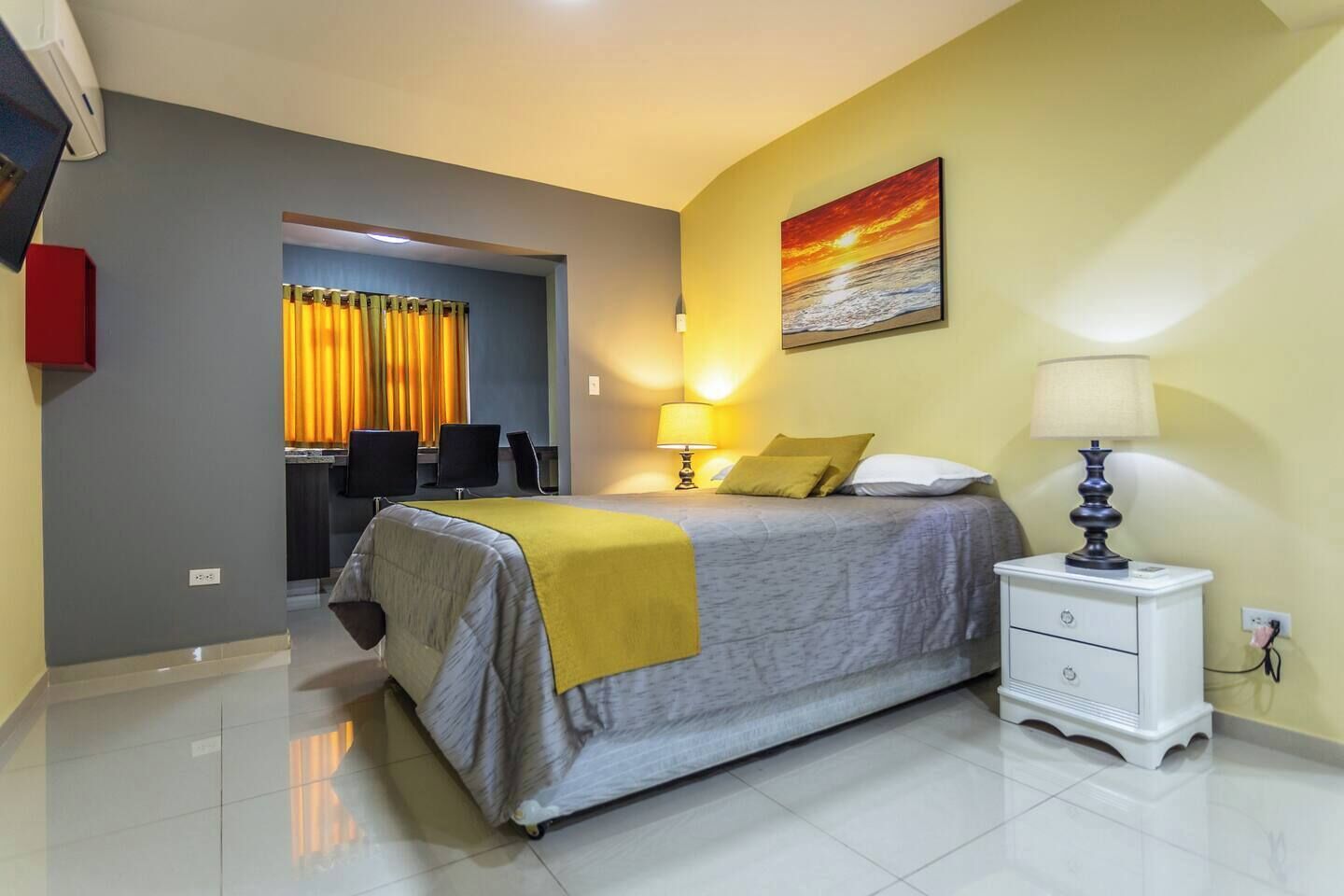 A hotel room with a bed, bedside table, and a painting on the wall.