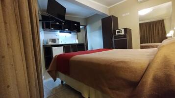 Una habitación de hotel con cama, televisor, kitchenette y microondas.