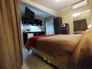 Quarto de hotel com cama, televisão, cozinha compacta e micro-ondas.