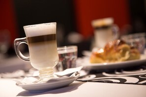 Uma chávena de café sobre um pires, com um fundo desfocado de um prato com comida e um copo.