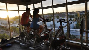 Un gimnasio con bicicletas estáticas y un amplio ventanal con vistas a un paisaje urbano.