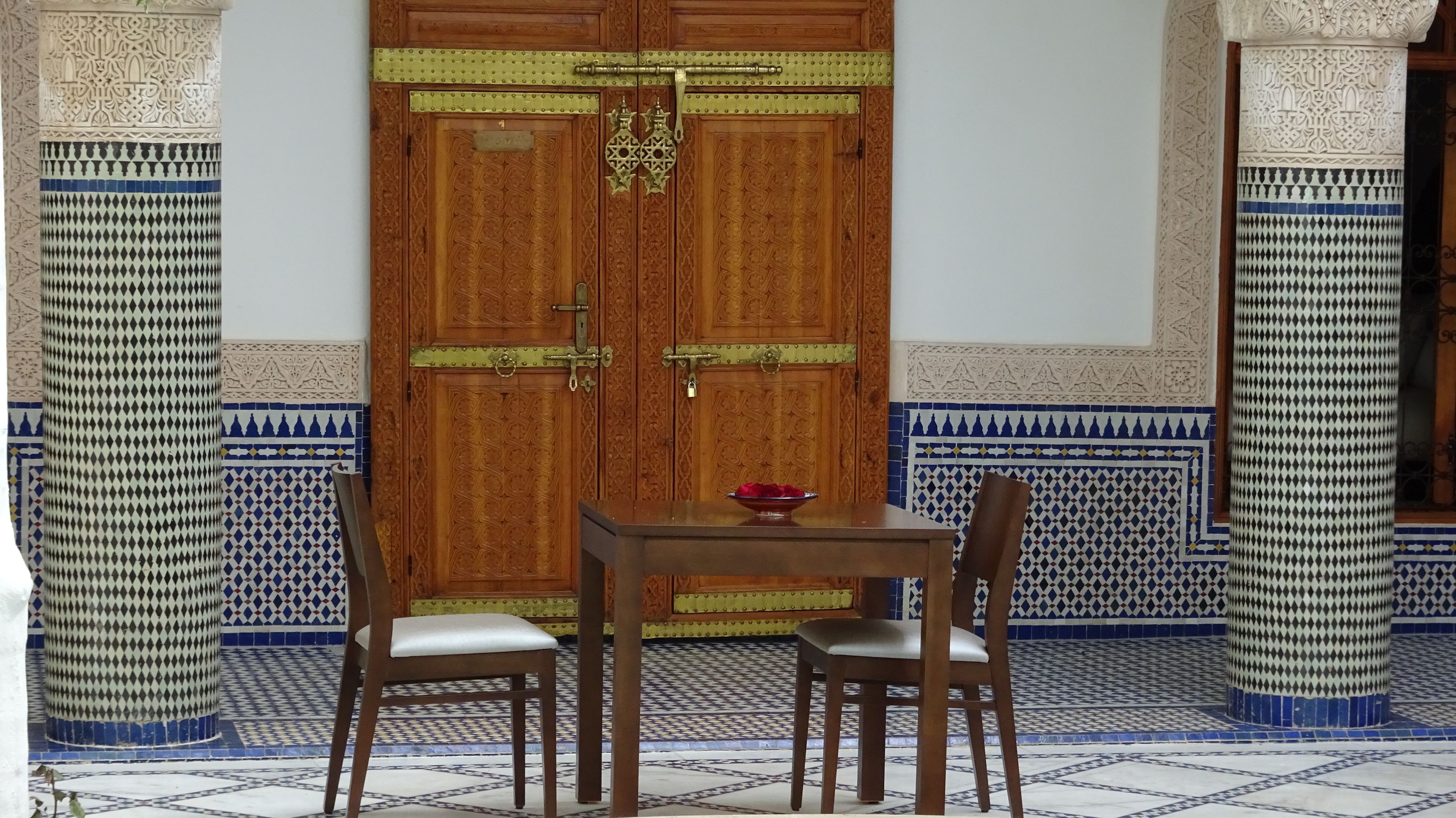 Une pièce au décor traditionnel, avec une porte en bois, deux chaises, une petite table et un bol décoratif.