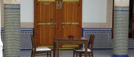 A traditional room with a wooden door, two chairs, a small table, and a decorative bowl.