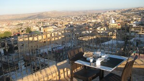 Terraço com mesa e cadeiras, com vista para um horizonte urbano com edifícios e colinas.