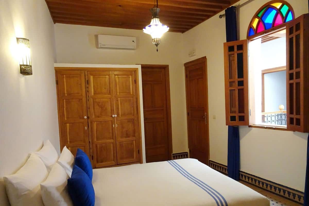 Un dormitorio con cama, armarios de madera, una araña y un ventanal de vitral.