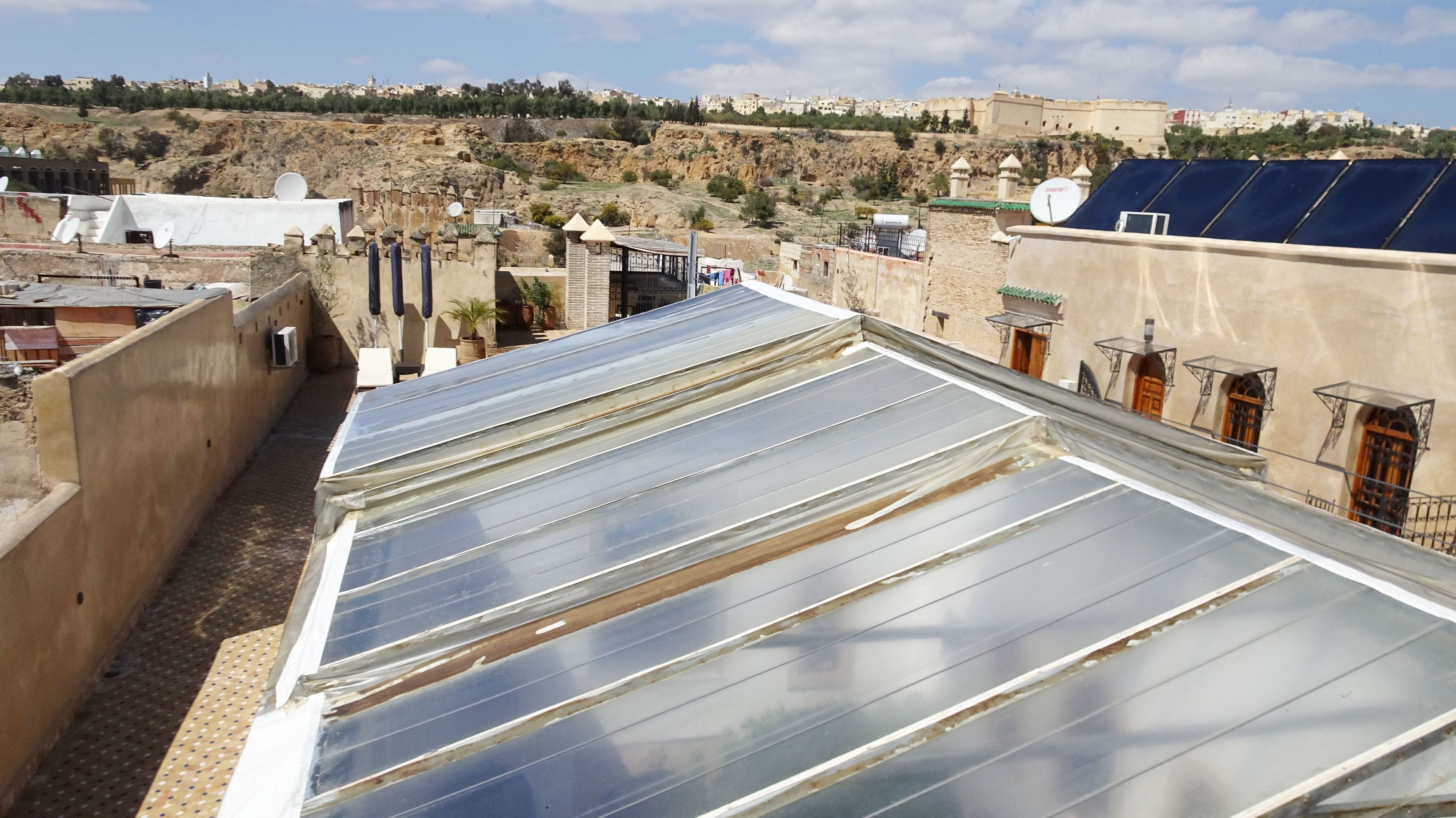 A rooftop with solar panels, a stone wall, and a view of a hillside with buildings.
