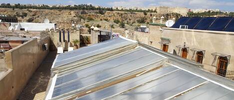 A rooftop with solar panels, a stone wall, and a view of a hillside with buildings.