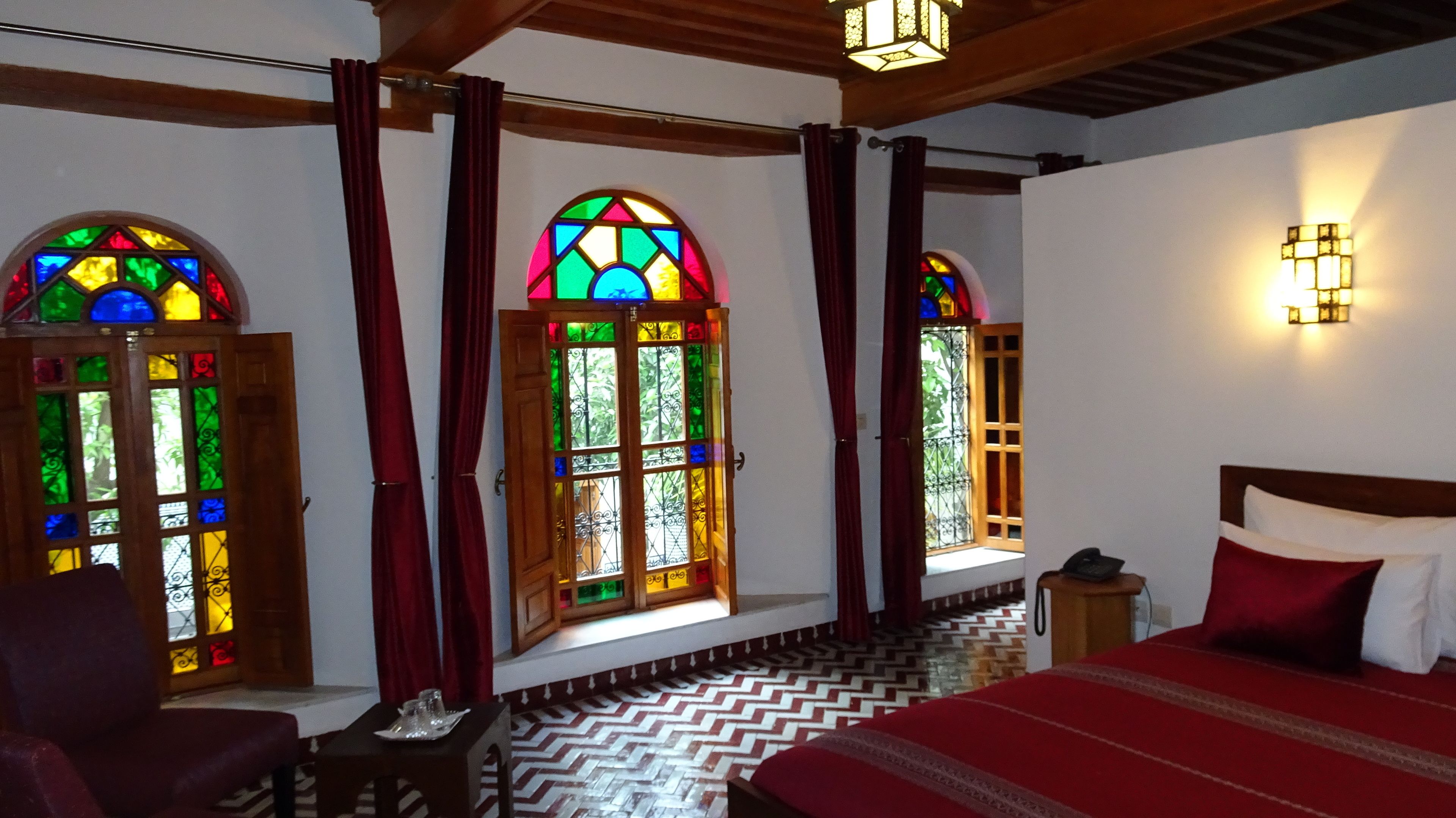 Une pièce comprenant un lit, une chaise, une petite table et une fenêtre ornée de vitraux.