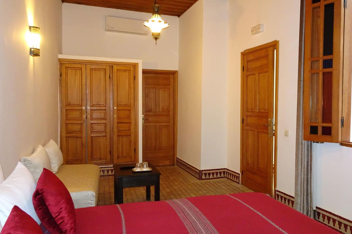 Un dormitorio con cama, almohadas, mesita de noche, espejo y puertas de madera.