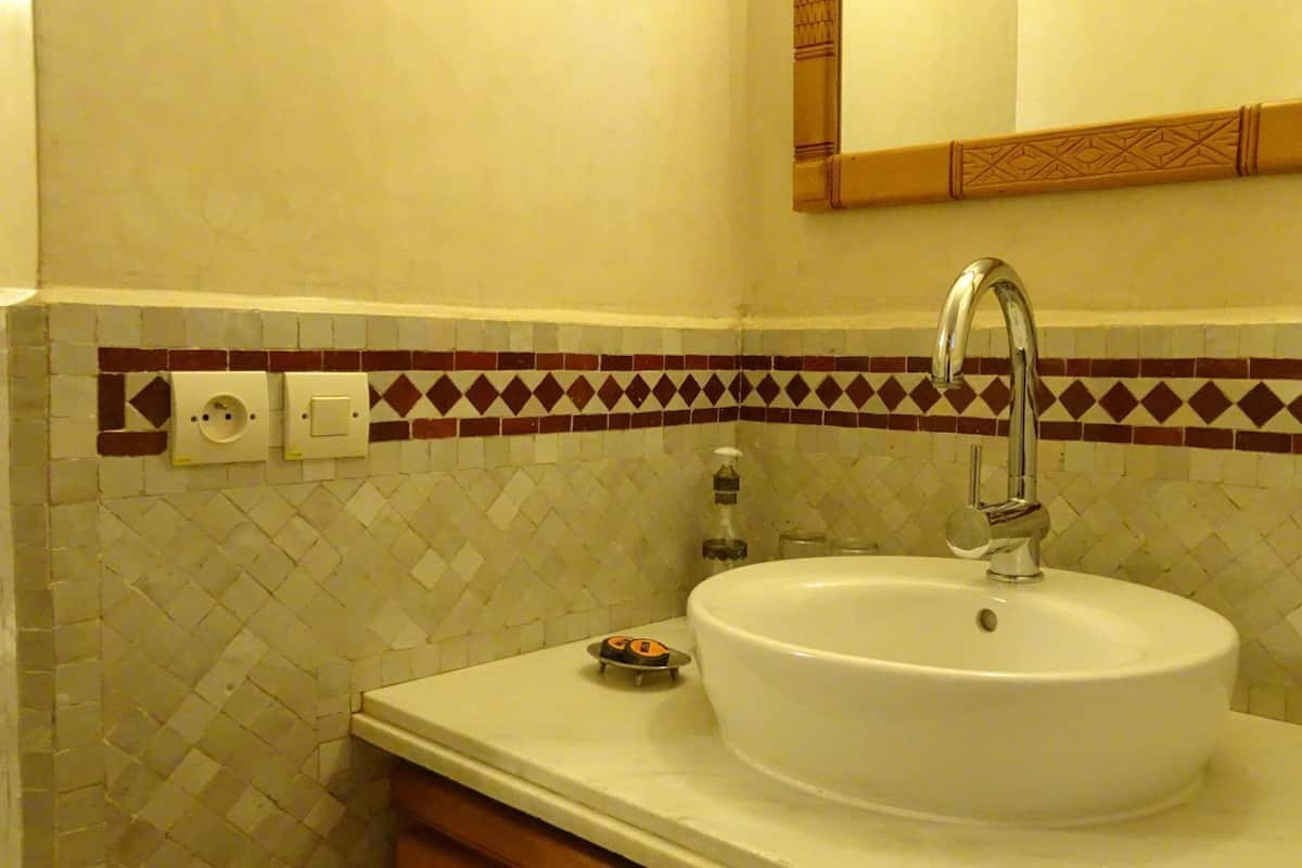 Un baño con un lavamanos blanco, un espejo encima y un salpicadero de azulejos estampados.