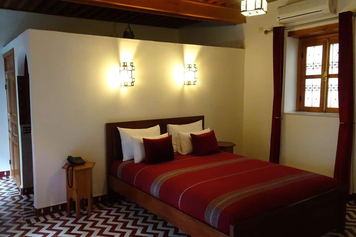 Un dormitorio con cama de madera, suelo estampado y dos luces fijadas a la pared.