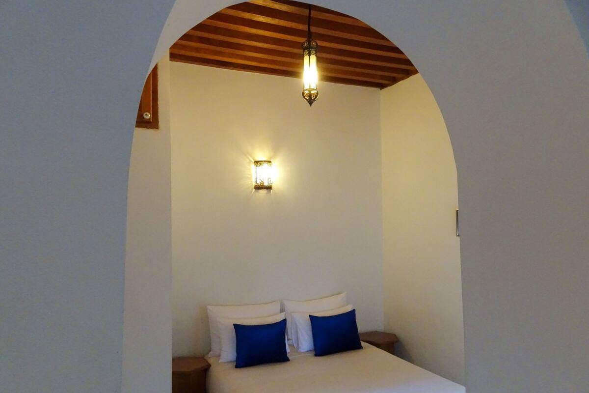 Un dormitorio con cama, dos mesitas de noche, lámpara de pared y techo abovedado.
