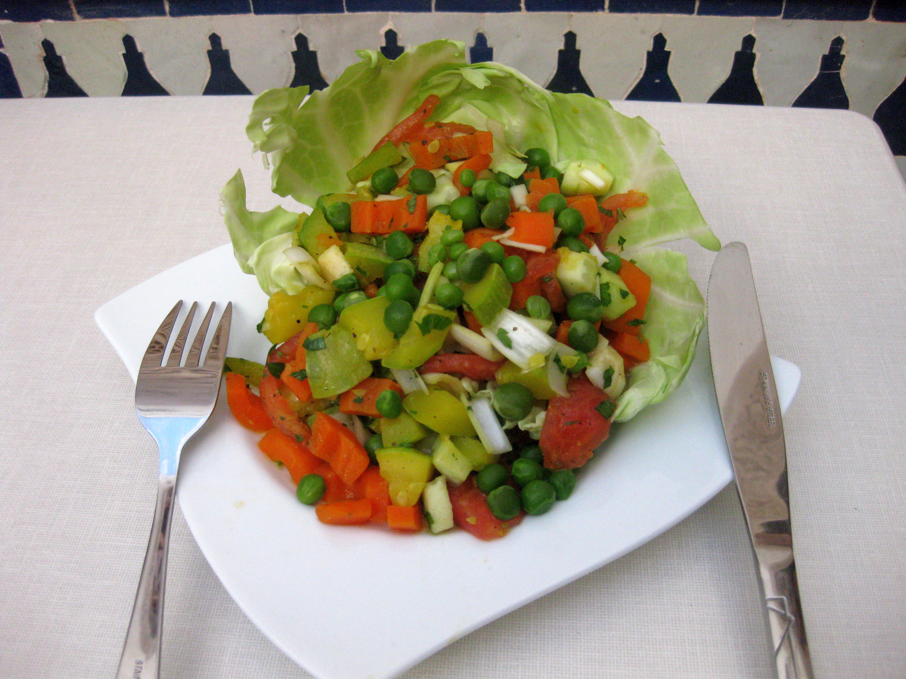 Une salade servie dans une assiette blanche, avec une fourchette et un couteau à côté.