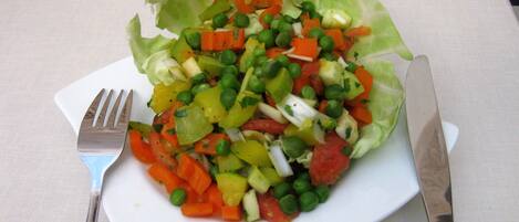 Une salade servie dans une assiette blanche, avec une fourchette et un couteau à côté.
