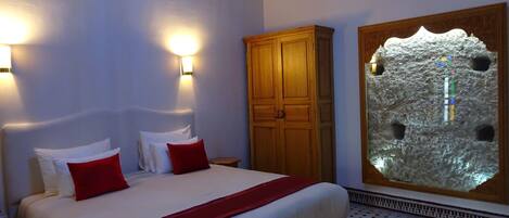 A hotel room with a bed, two wall-mounted lights, a wooden wardrobe, and a decorative stone wall.
