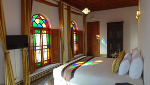Um quarto com cama, televisão e janelas de vitrais.