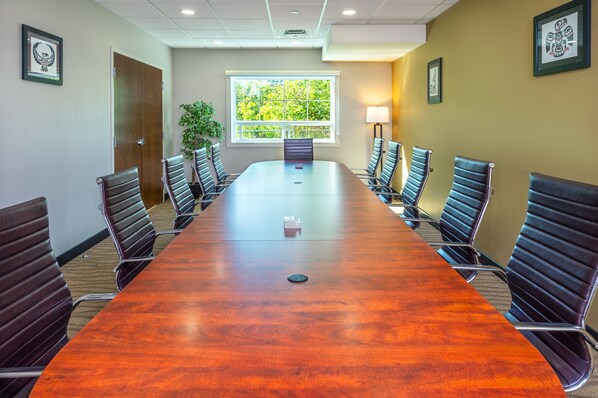 A conference room with a long wooden table, black leather chairs, a window with a view of trees, and framed artwork on the walls.