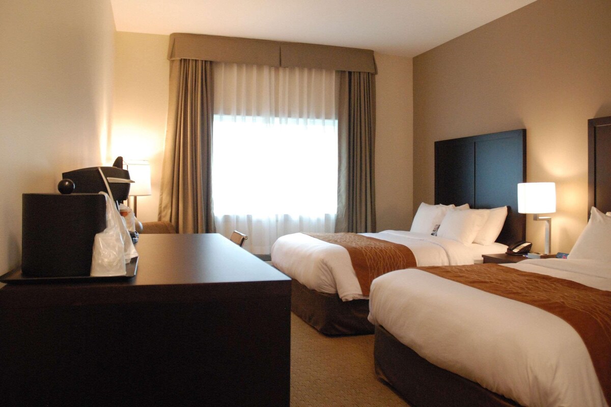 Habitación de hotel con dos camas, un escritorio, una lámpara y un ventanal con cortinas.