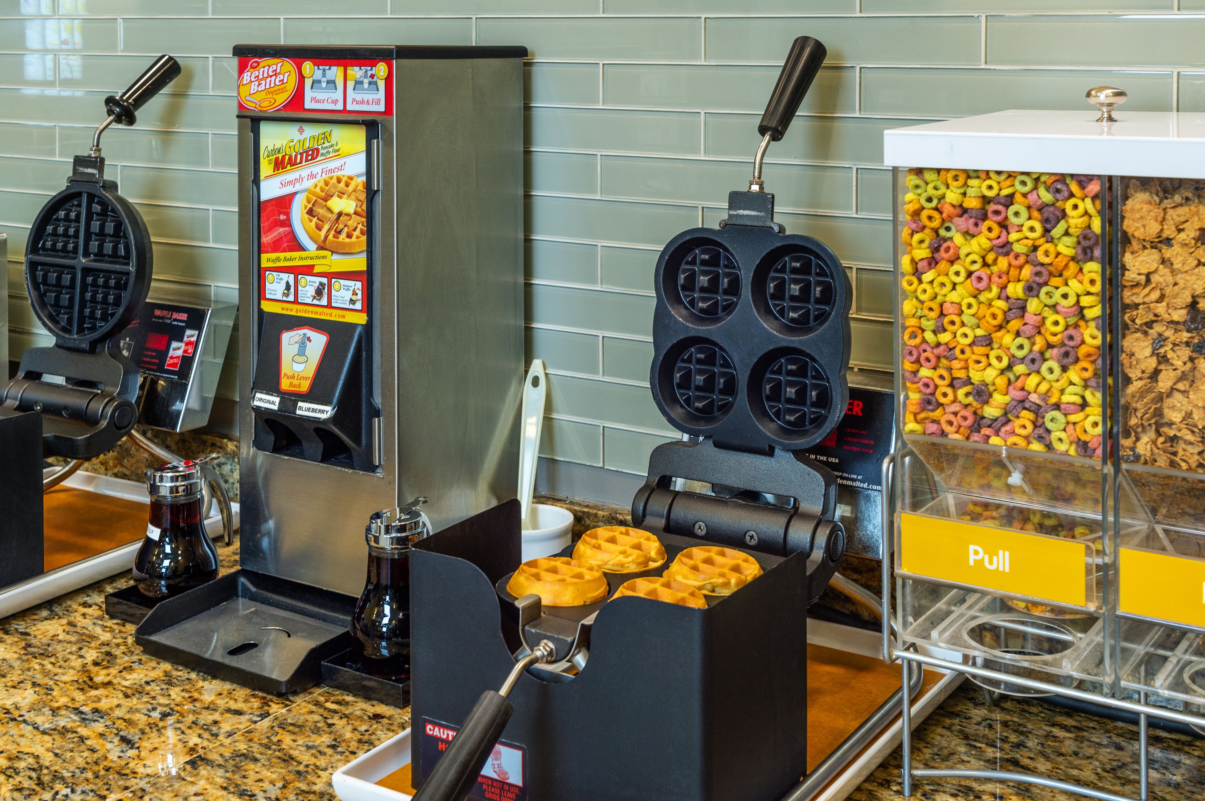 Two waffle makers and a container of cereal.