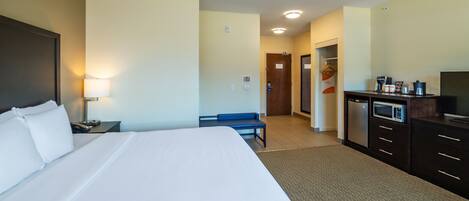 A hotel room with a large bed, a desk with a lamp, a microwave, and a coffee maker.