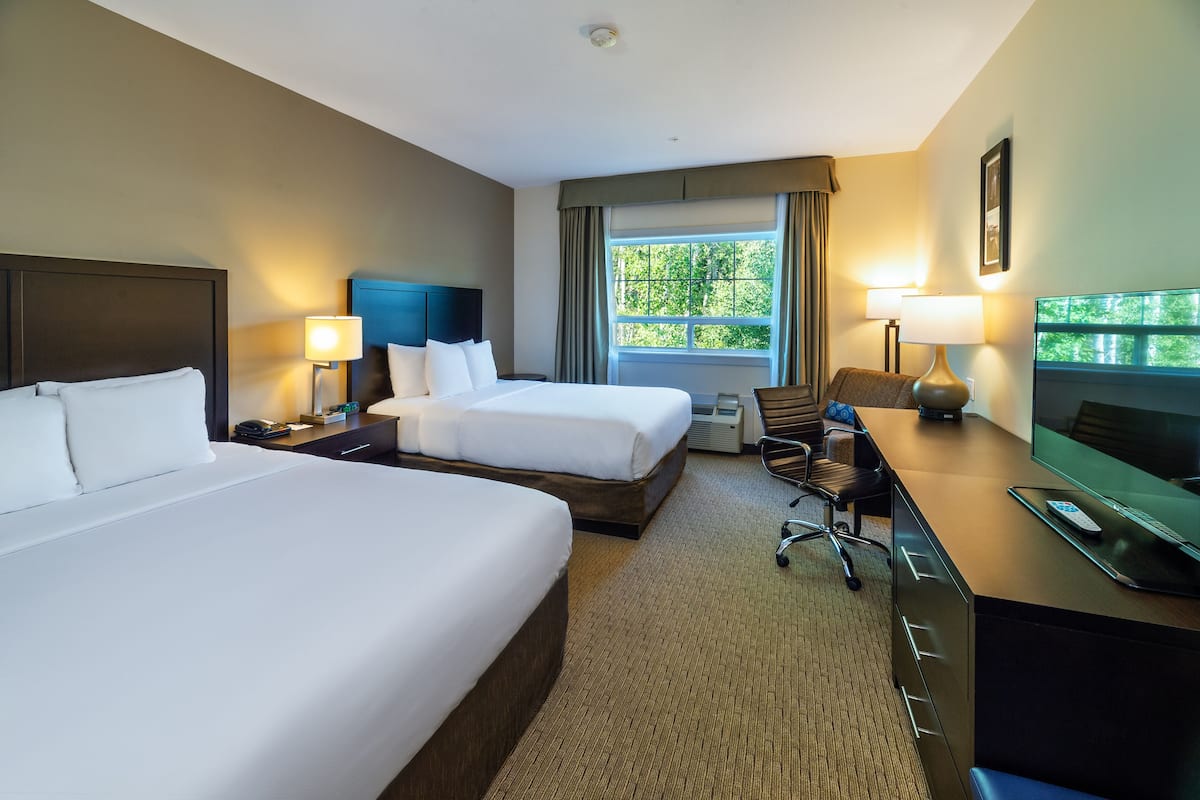 A hotel room with two beds, a desk with a TV, and a window with curtains.