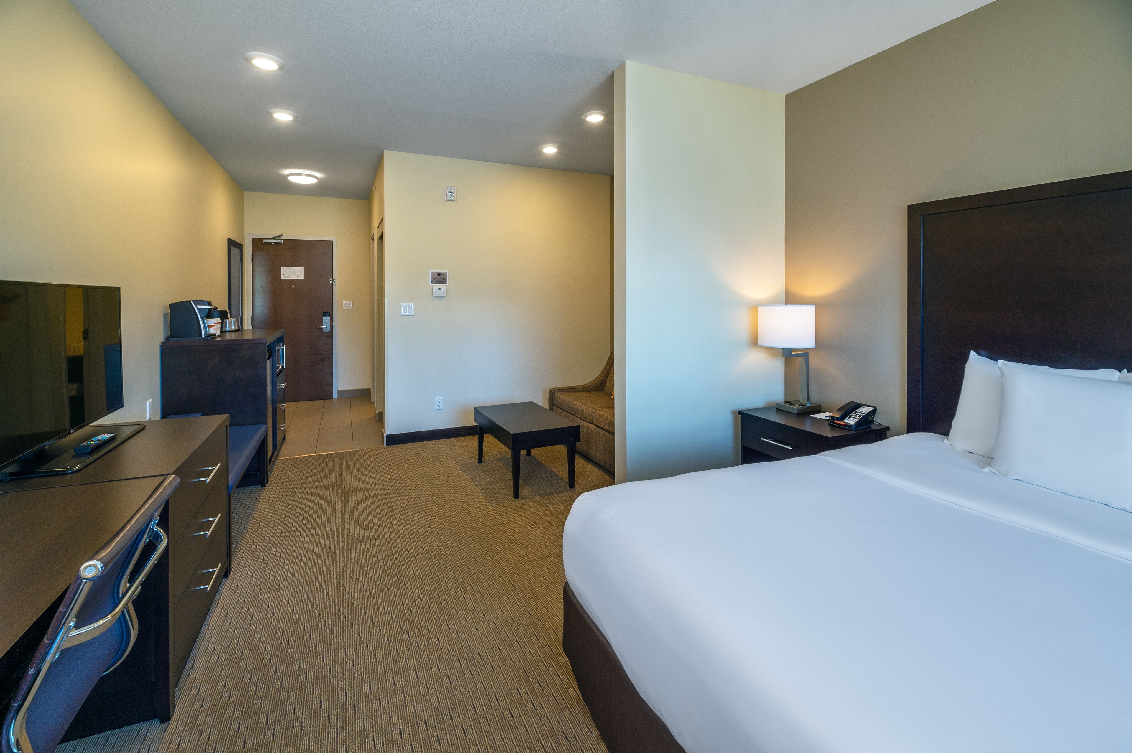 A hotel room with a bed, desk, chair, and a small table.