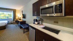 A compact hotel room with a kitchenette including a microwave, a coffee maker, and a dishwasher. There is a bed, a desk, and a chair. - Comfort Inn & Suites (Terrace)