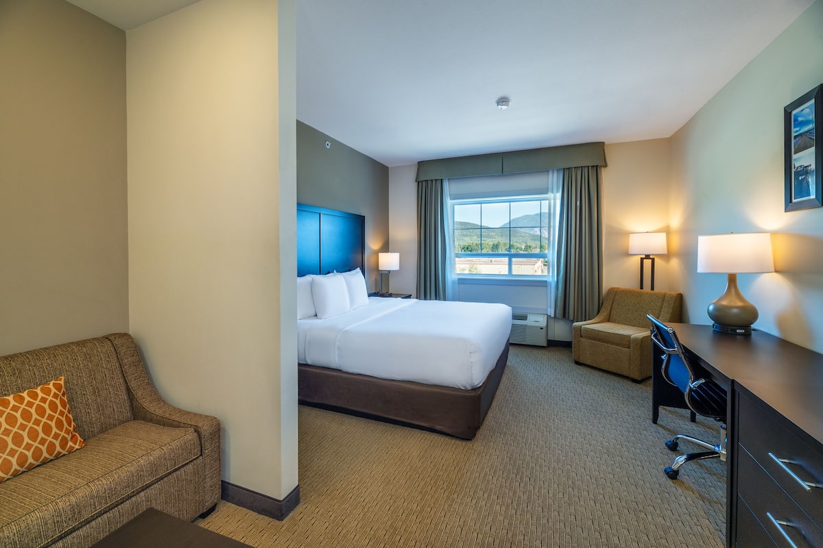A hotel room with a large bed, a sofa, a desk, and a chair.