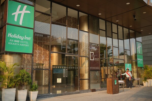 Het uiterlijk van Holiday Inn Kolkata Airport met grote glasramen, een beveiligingsbeambte en een bordje dat aangeeft dat het een IHG hotel is.
