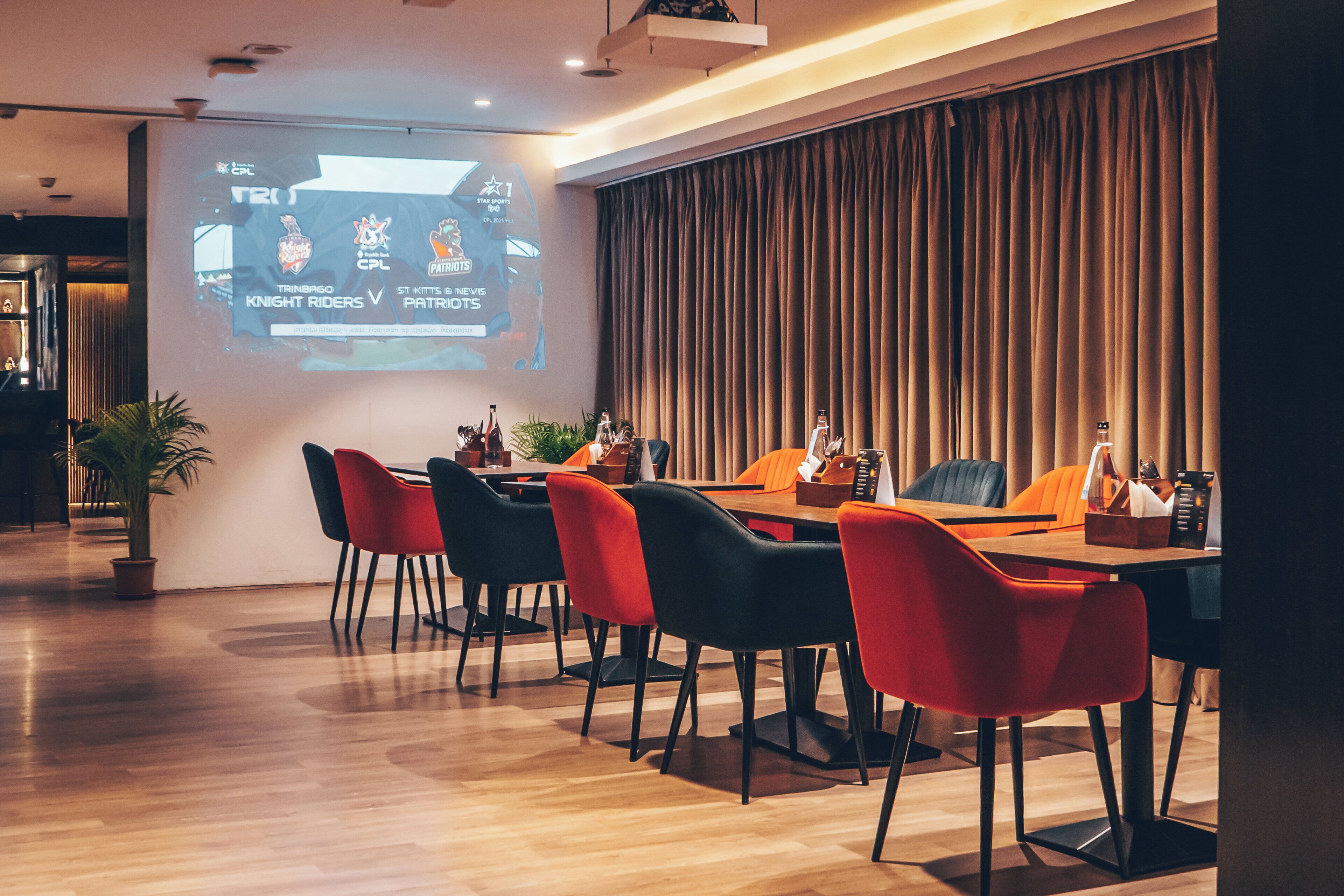 A conference room with a projection screen displaying a sports match, a wooden table, and modern chairs.