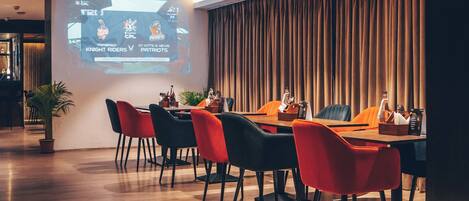A conference room with a projection screen displaying a sports match, a wooden table, and modern chairs.