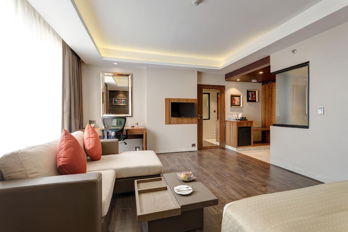 A hotel room with a sofa, a desk, a bed, and a small table with a plate and a bowl.