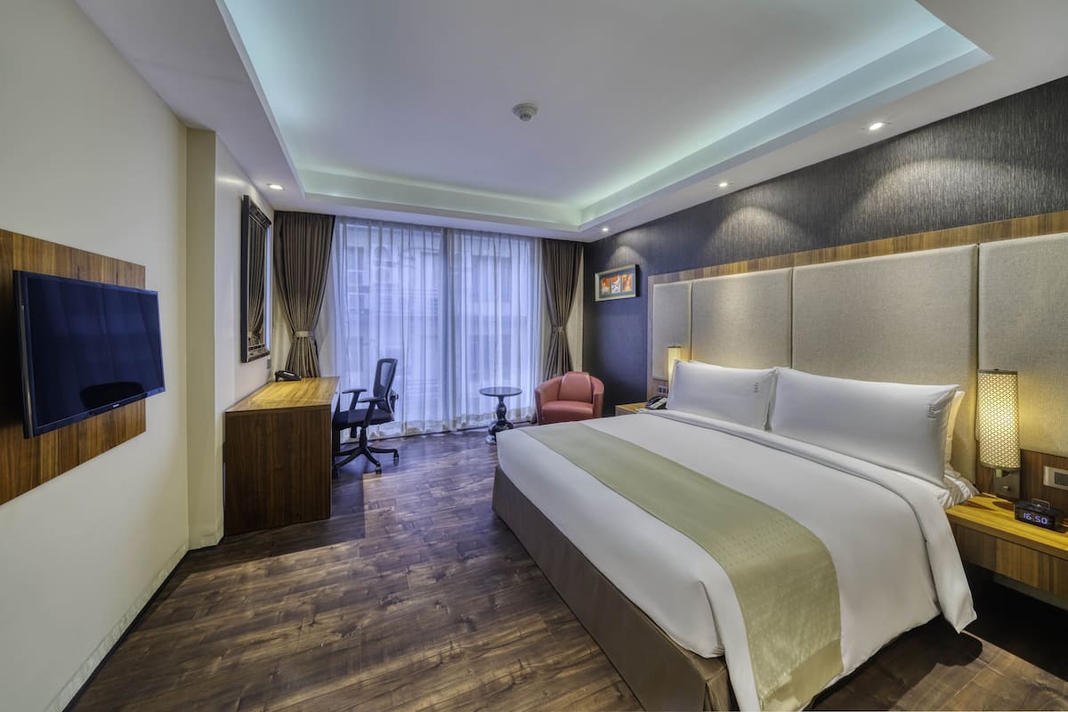 A hotel room with a large bed, a desk, a chair, a TV, and a window with curtains.