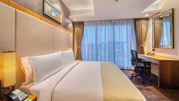 A hotel room with a large bed, a desk, a chair, a phone, and a window with curtains.
