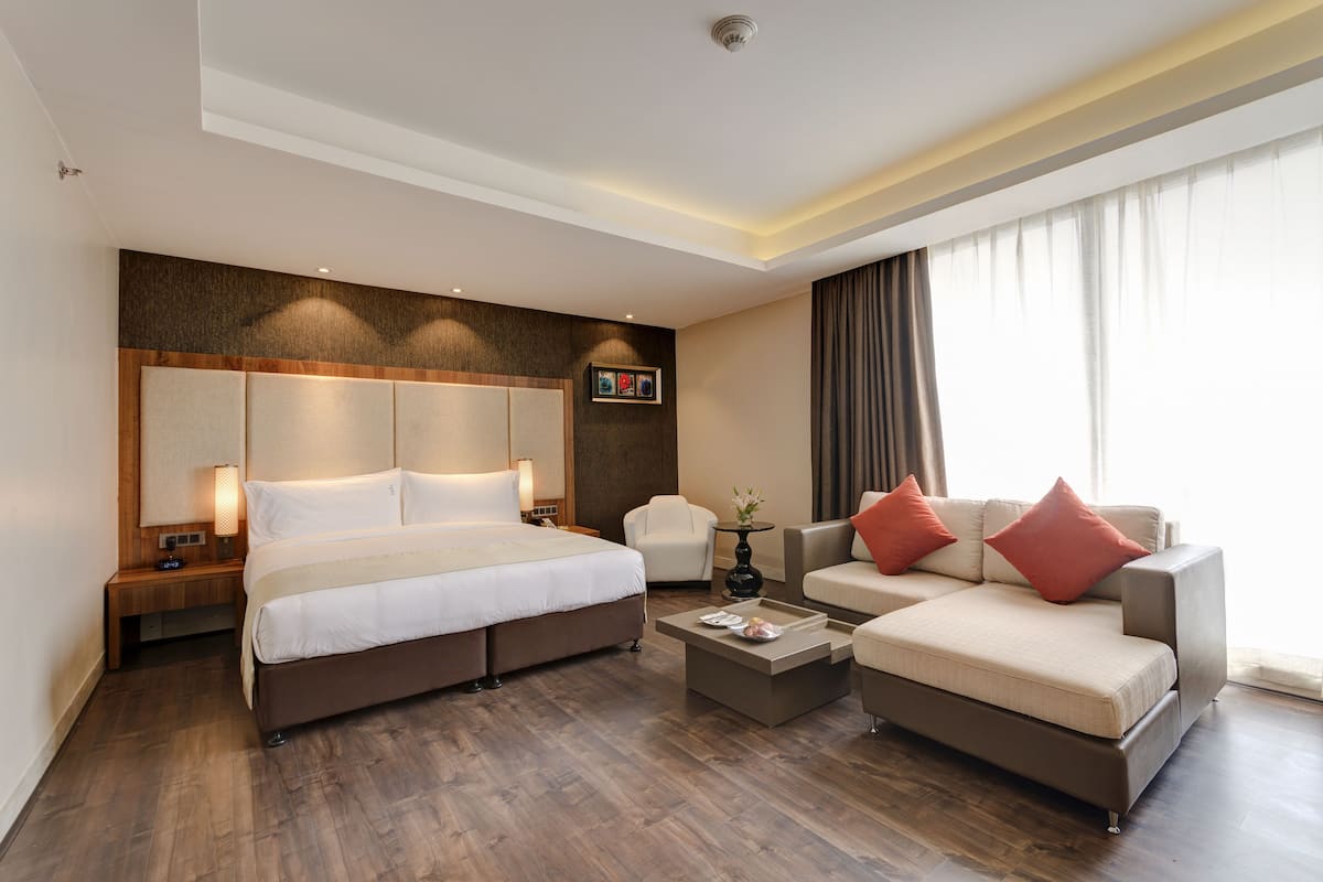 A modern hotel room with a large bed, a sofa, a coffee table, and a chair.