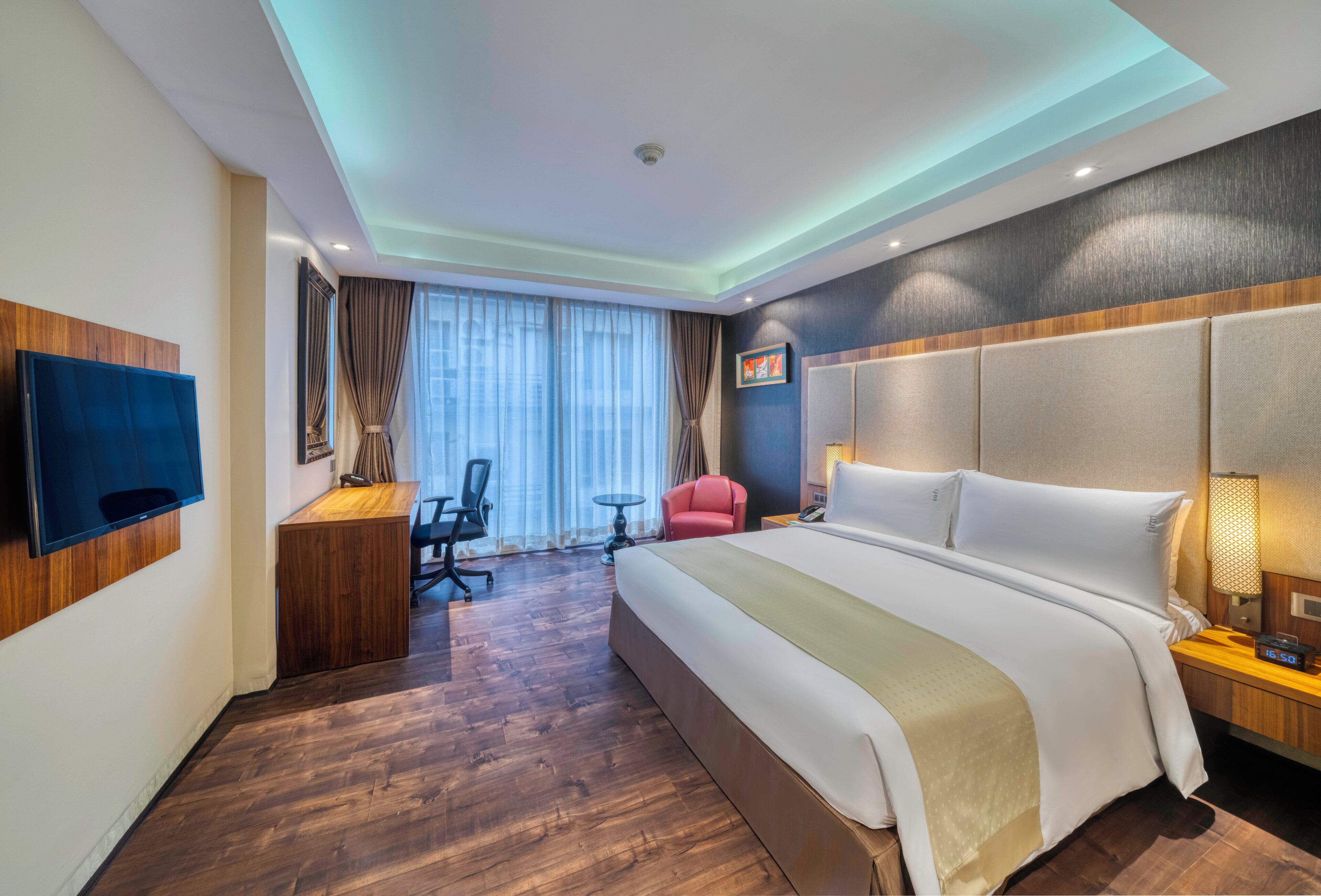 Habitació d'hotel amb llit, escriptori, cadira i televisió penjada a la paret.