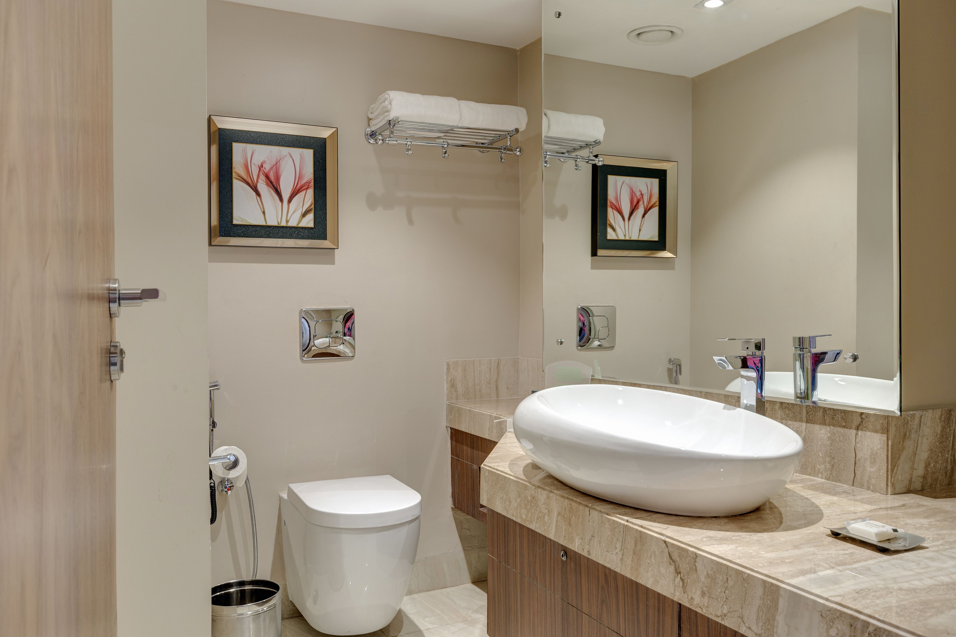 Un baño moderno con un lavamanos grande blanco, un inodoro, un perchero para toallas y dos cuadros enmarcados en la pared.
