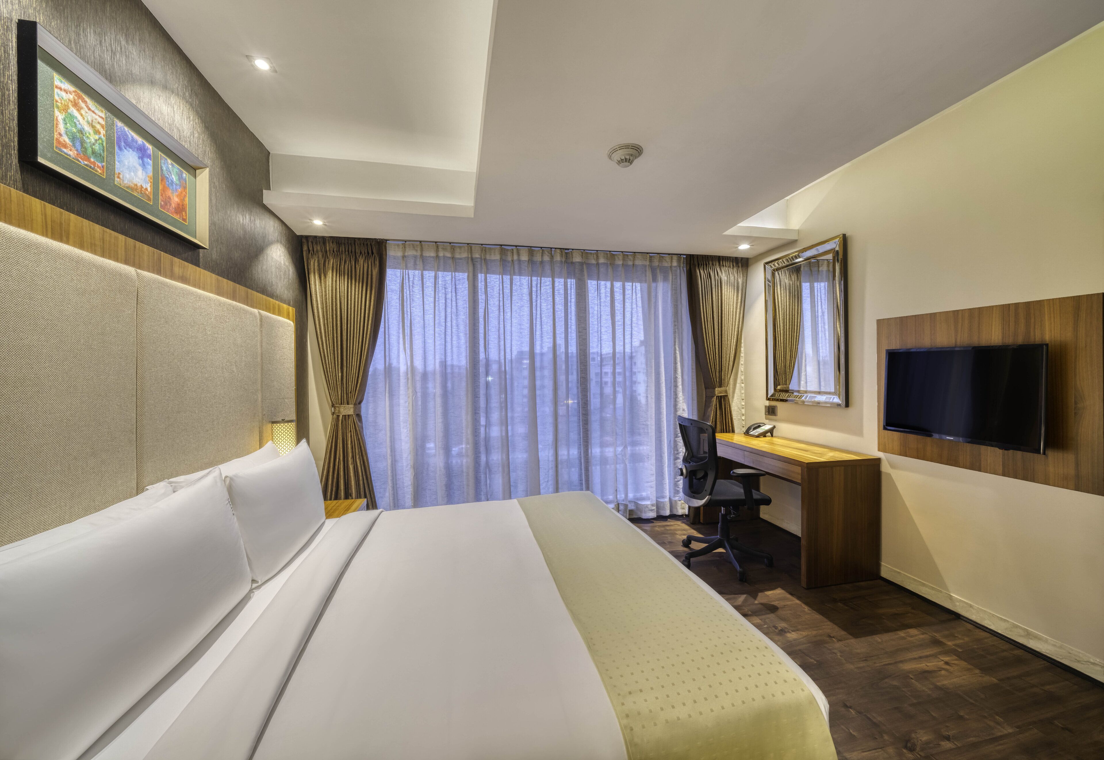 Una habitación de hotel con una cama grande, un escritorio, una silla, un televisor y una ventana con cortinas.