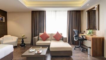 A modern hotel room with a sofa, a desk, a chair, a coffee table, and a bed.